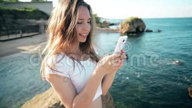 在海滩日落时，智能手机女人用智能手机短信。 混合